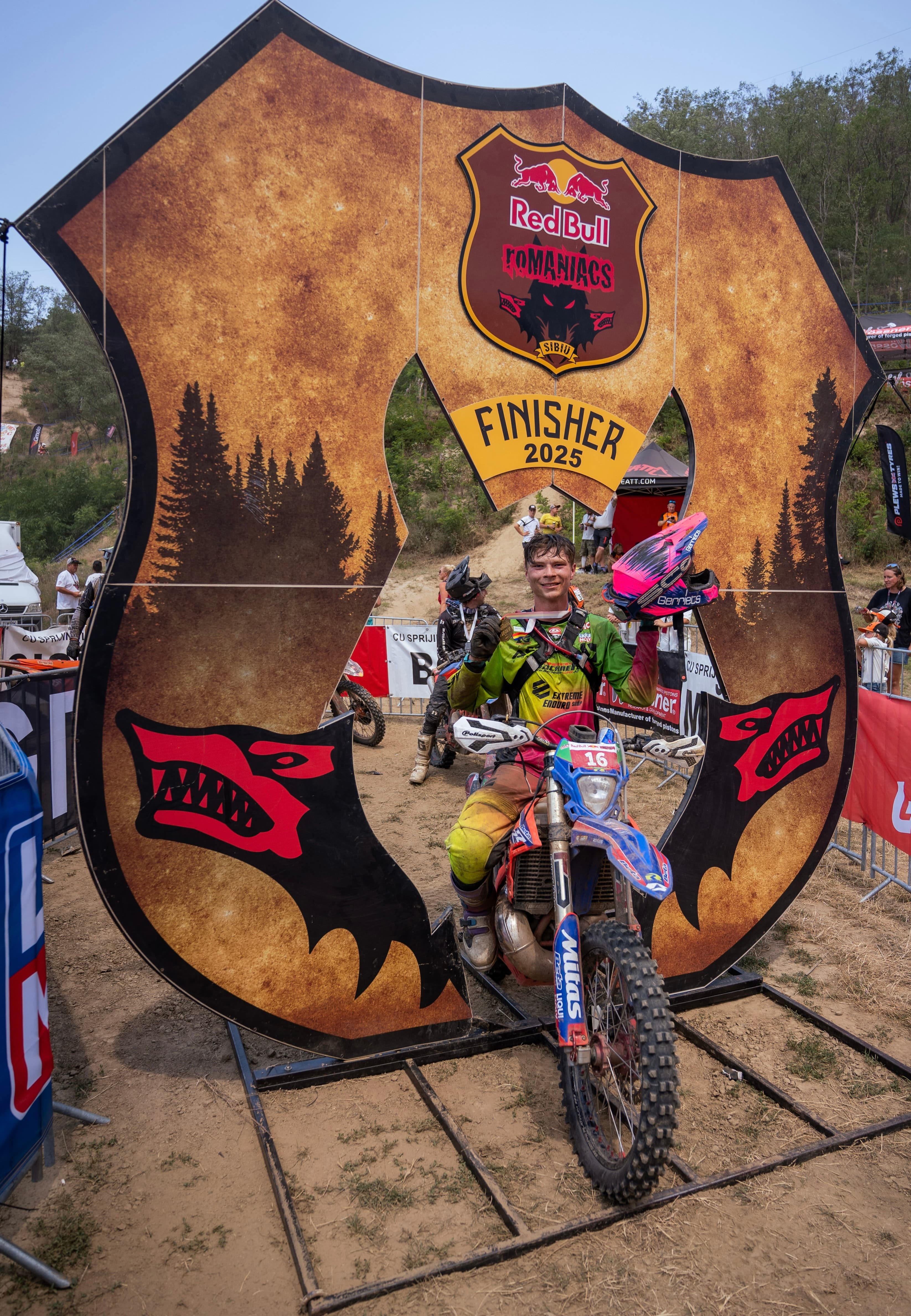 Ein Motocross-Fahrer auf seinem blauen Motorrad posiert in einem großen Red Bull Romaniacs Finisher-Rahmen.