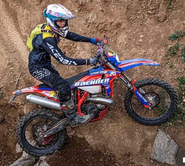 Ein Enduro-Fahrer auf einem rot-blauen Motorrad erklimmt konzentriert einen steilen, steinigen Hang.