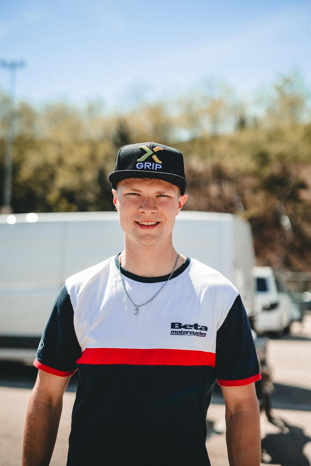 Lächelnder Mann mit X-Grip Kappe und Beta Motorcycles T-Shirt vor einem weißen Transporter.