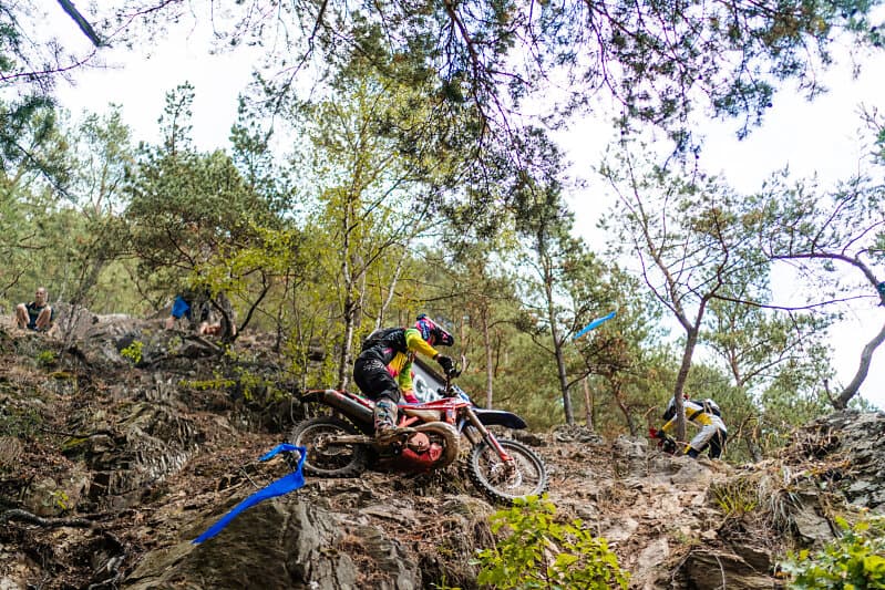 Motocross-Fahrer navigiert sein Motorrad über steile Felsen und Wurzeln einen bewaldeten Hang hinauf.